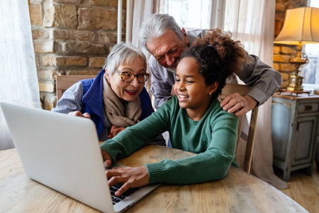 Joyful multiethnic grandparents with grandchild watching online game on laptop at home togetherの写真素材