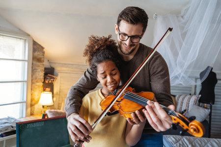 Music is so much fun. Young father teaching his little daughter to play violin and smiling.の写真素材