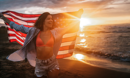 Young woman holding national American flag walking ocean beach. America Independence Day conceptの写真素材