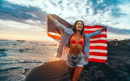 Happy woman holding american USA flag and running on the beach. Independence Day, travel conceptの写真素材