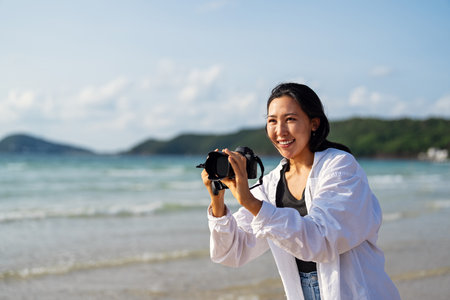 A joyful woman embraces the freedom of beach life, enjoying the fresh ocean breeze with her camera