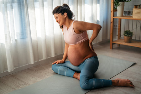 Young pregnant female feeling pain, suffering from abdominal ache at home during yoga exercise