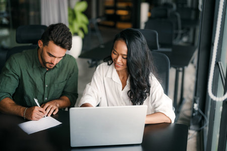 Multiracial colleagues discussing startup project and smiling during workday in office interiorの写真素材