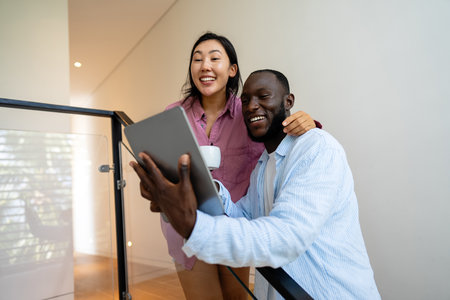 Young happy multiethnic couple having fun while using laptop at home. Happy couple discussing futureの写真素材