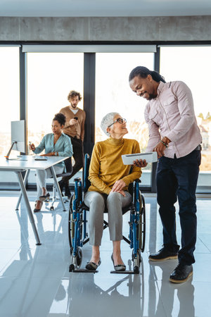 Business woman in wheelchair working with colleague in modern inclusive office. Diversity, supportの写真素材