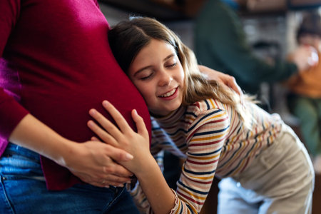 Daughter hugging, touching pregnant mothers belly. Little girl is looking at moms belly with loveの写真素材