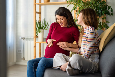 Daughter hugging, touching pregnant mothers belly. Little girl is looking at moms belly with loveの写真素材