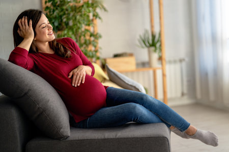 Happy expectant mother sitting on bed, feeling kicks, caressing belly smiling. Motherhood, pregnancyの写真素材