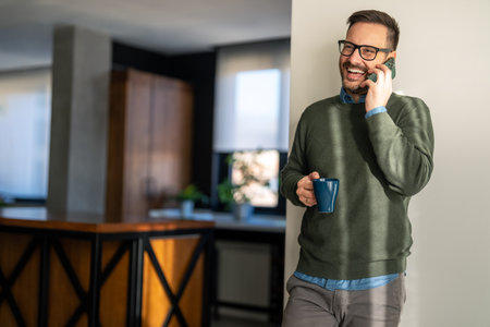 Happy smiling man wearing casual clothes and using modern smartphone in his home officeの写真素材