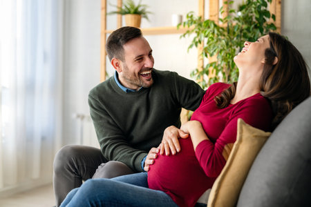Beautiful young couple with pregnant wife at home with her husband touching his wifes bellyの写真素材