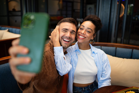 Diverse couple on a foodie date enjoys casual dining and a phone moment, sharing sunny vibes, drinksの写真素材