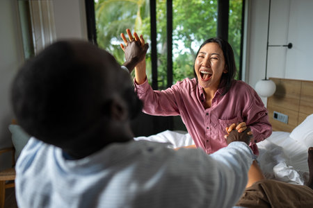 Young diverse couple joyfully smiling together in their bright living room, wearing casual clothesの写真素材