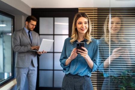 A confident businesswoman leads her busy office life, multitasking with smartphone communicationの写真素材