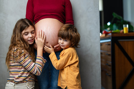 Cute siblings happily awaiting a new family member to come. They touching their mothers belly.の写真素材