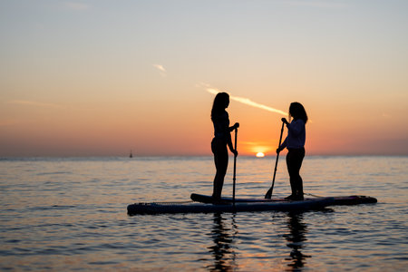 Group enjoying paddle boarding in sunset light reflects an active holiday filled with adventureの写真素材