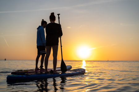 Group enjoying paddle boarding in sunset light reflects an active holiday filled with adventureの写真素材
