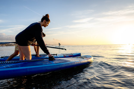 Two people resting by their paddleboards as the sun sets create a mindful outdoor momentの写真素材