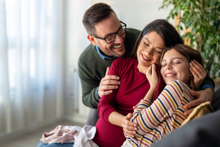 Happy family with pregnant mother sitting on sofa, having fun with joyful kid, waiting for babyの写真素材