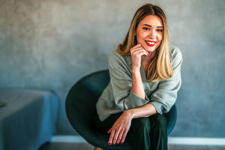 A relaxed caucasian woman smiling in a soft, modern interior, creating a warm lifestyle portraitの写真素材