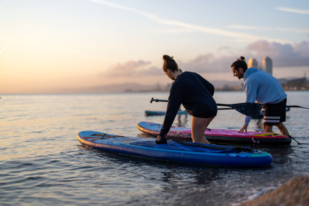 Couple of tourists young man and woman having fun paddle boarding at sea