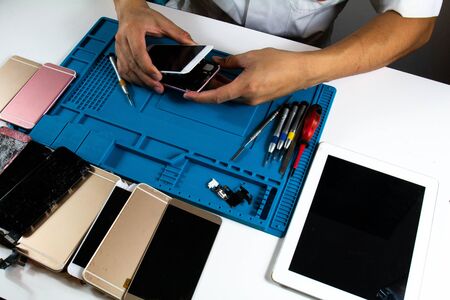 The mobile phone repairman has completed the repair. He is assembling the mobile phone screen.の写真素材