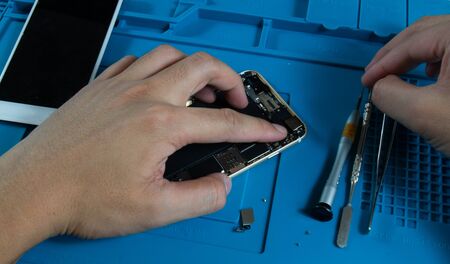 A mobile repairman is assembling a new mobile phone camera with a mobile phone after he has already replaced the new parts.の写真素材