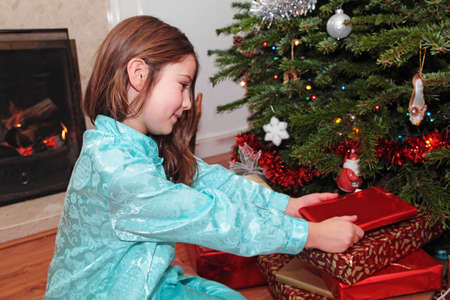 A girl opening Christmas presents under a Christmas tree with a log fire in the backgroundの写真素材