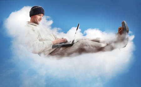 A man on a cloud operating a laptop.  The man is dressed casually to represent the majority of IT workers.  The concept is Cloud Computing - software/computing in the cloud.の写真素材