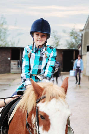 A pretty girl preparing to ride, stables in the background and somebody tightening the horse's girth.の写真素材