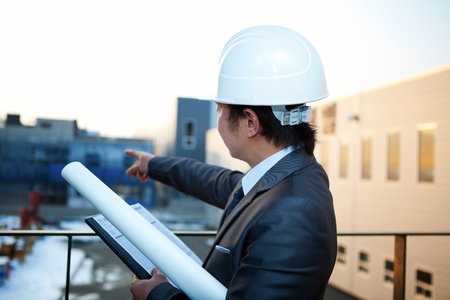 young architect with white helmet holding blueprint and clipboard pointing at the buiding constructionの写真素材