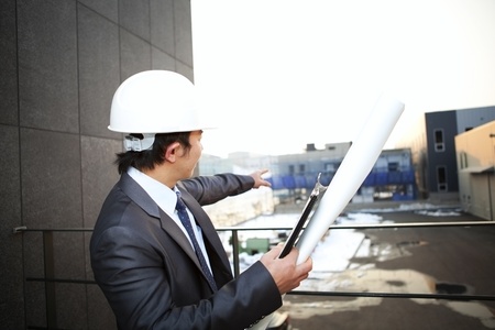 young architect with white helmet holding blueprint and clipboard pointing at the buiding constructionの写真素材