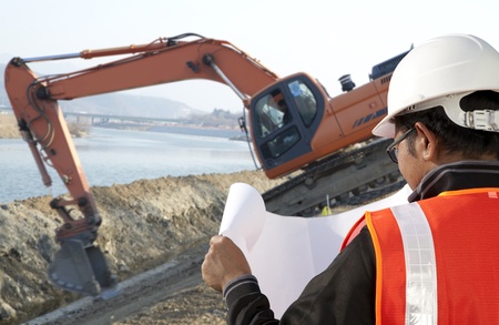 foreman construction in front of excavator checking plan の写真素材