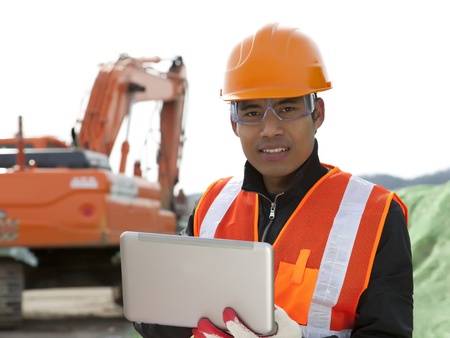 road construction worker using laptop standing front excavatorの写真素材