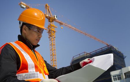 construction worker checking a blueprint with crane on the backgroundの写真素材