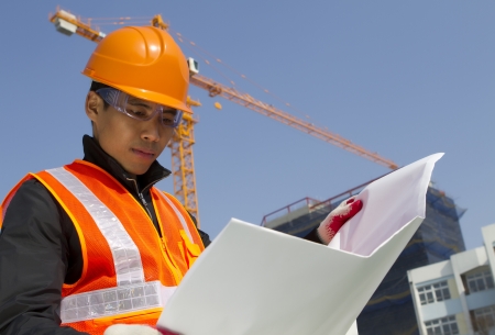 construction worker checking a blueprint with crane on the backgroundの写真素材