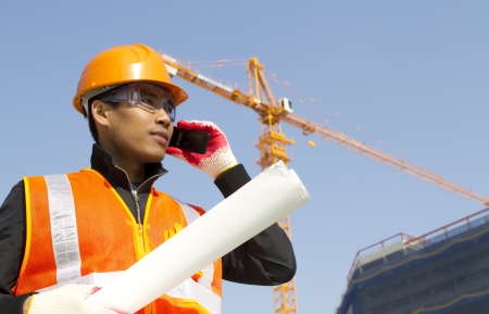 construction worker talking in mobile phone with crane in backgroundの写真素材