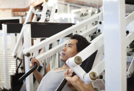 asian man exercising on machines at modern gym - health club