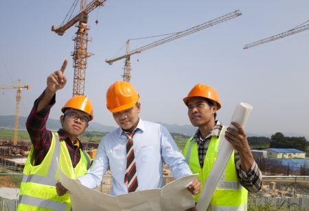 Architect and construction workers discussion on site with yellow cranes on the backgroundの写真素材