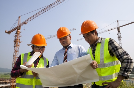 Architects at a construction site looking at blueprint discussion under cranesの写真素材