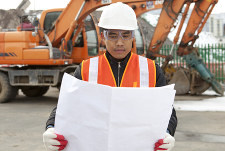 Architect looking at blueprints with excavator on backgroundの写真素材