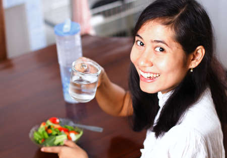 Portrait of smiling young woman drinking water with salad on tableの写真素材