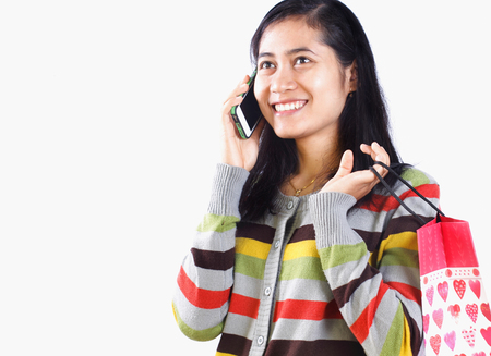Asian woman carrying shopping bag and talking on mobile phone isolated on white backgroundの写真素材