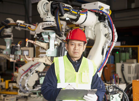 Manufacture worker holding a notepad with robot machine on backgroundの写真素材