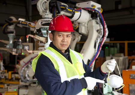 Factory worker pointing safety mask with robot machine on the backgroundの写真素材