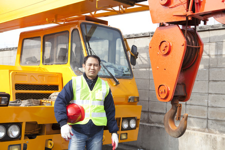 Driver crane truck posing next to the huge mobile crane with holding safety helmet