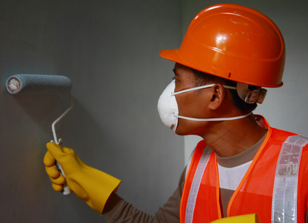Painter worker wearing safety mask or safety work on job, painting of building house or apartment wall with rollの写真素材