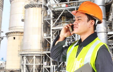 Industrial engineer standing in front of a large oil refinery conversation via phoneの写真素材