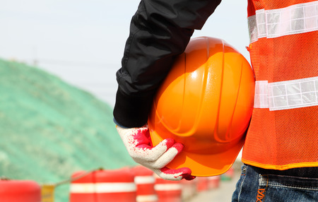 Close-up construction worker with safety vest holding hardhat on location site. Construction safety conceptの写真素材