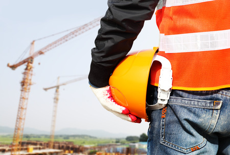 Construction safety concept, close-up worker holding hardhat with crane in the backgroundの写真素材