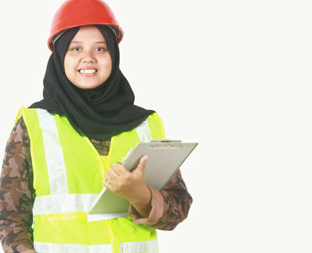 Smiling  young worker woman muslim holding a notepad and using safety vest with isolated white backgroundの写真素材
